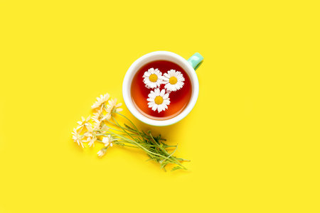 Cup of natural chamomile tea and flowers on yellow backgroundの写真素材