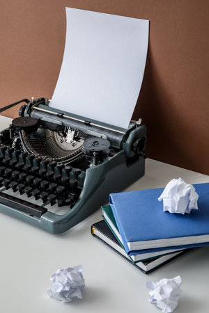 Vintage typewriter with books and crumpled paper on white table near brown wall