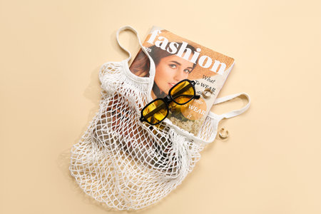 Stylish sunglasses and string bag with magazine on beige backgroundの写真素材