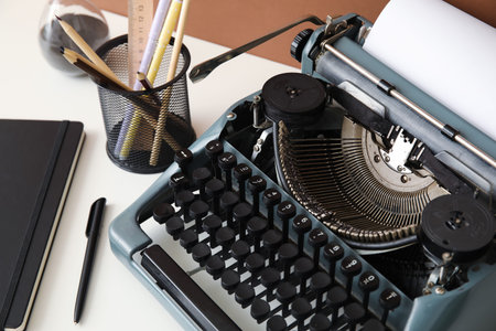 Vintage typewriter with pencil holder, hourglass and notebook on white table near brown wall