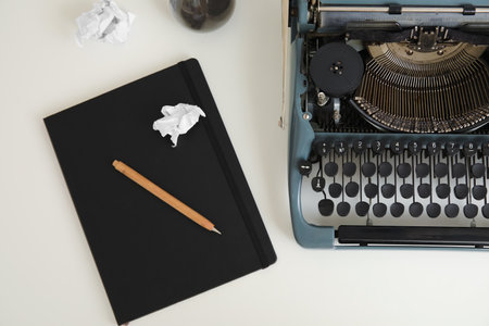 Vintage typewriter with hourglass and notebook on white table near wallの写真素材