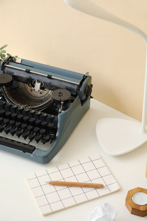 Vintage typewriter with lamp, notebook and candle on table near beige wallの写真素材