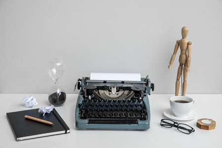 Vintage typewriter with cup of coffee, wooden mannequin and notebook on white table near wallの写真素材