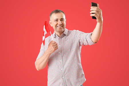 Mature man with flag of Canada taking selfie on red backgroundの写真素材