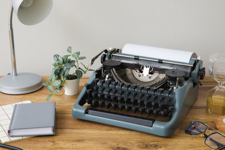 Vintage typewriter with hourglass, lamp and notebooks on brown wooden table near wallの写真素材