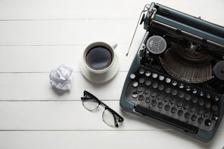 Vintage typewriter with cup of coffee, eyeglasses and crumpled paper on white wooden background
