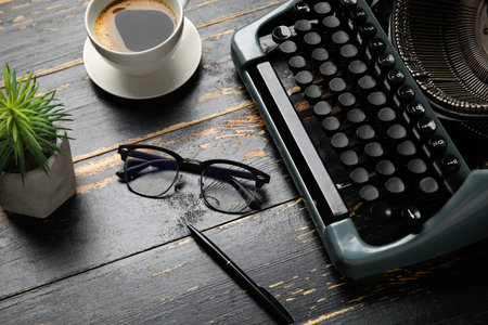 Vintage typewriter with cup of coffee, eyeglasses and houseplant on dark wooden background