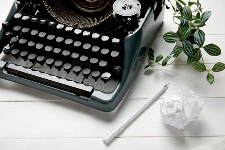 Vintage typewriter with pen, houseplant and crumpled paper on white wooden background