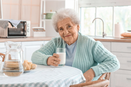 Senior woman with glass of milk in the kitchenの写真素材
