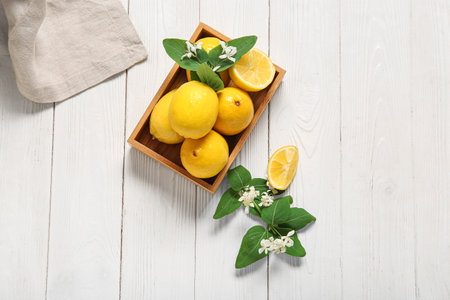 Wooden box of lemons with blooming branches on white tableの写真素材