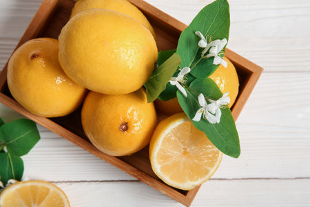 Wooden box of lemons with blooming branches on white tableの写真素材