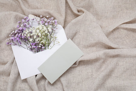 Envelope with beautiful gypsophila flowers and blank invitation card on gray crumpled tablecloth