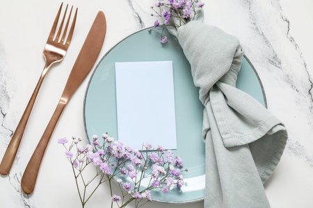 Clean plate with blank invitation card, cutlery and gypsophila flowers on white tableの写真素材