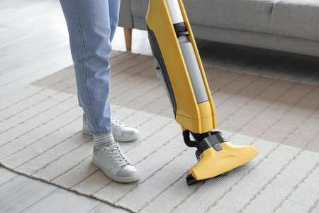 Young woman hoovering carpet at home, closeupの写真素材