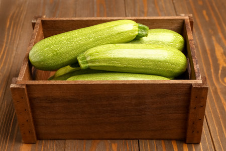 Box with fresh green zucchini on wooden backgroundの写真素材