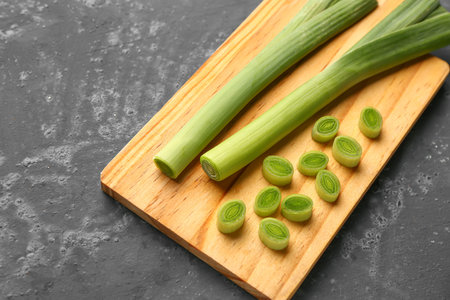 Board with fresh leeks on dark background