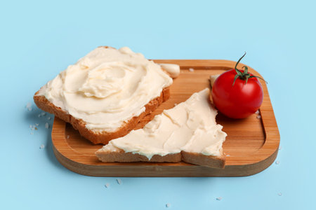 Wooden board of tasty toasts with cream cheese on blue backgroundの写真素材