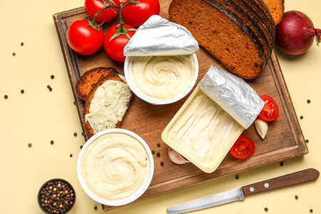 Wooden board with boxes of processed cheese, toasts and vegetables on pale yellow backgroundの写真素材
