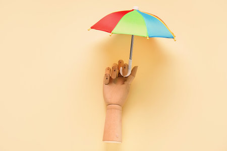 Creative composition with wooden hand and mini umbrella on pale yellow backgroundの写真素材