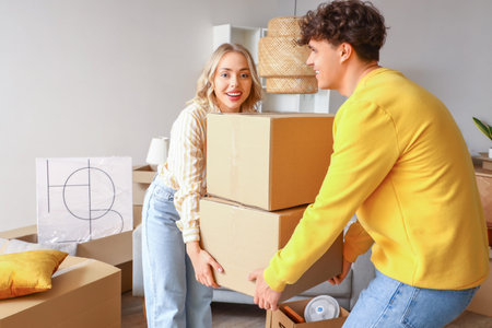 Young couple carrying cardboard boxes in room on moving day