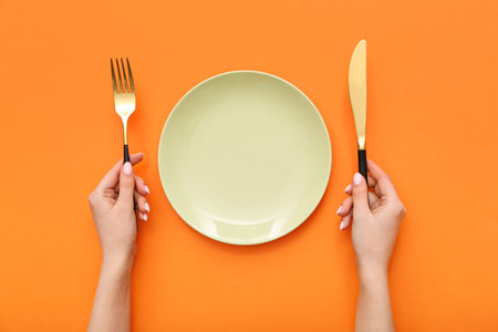 Female hands with cutlery and empty plate on orange backgroundの写真素材