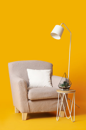 Cozy beige armchair, lamp and table with houseplant on orange backgroundの写真素材