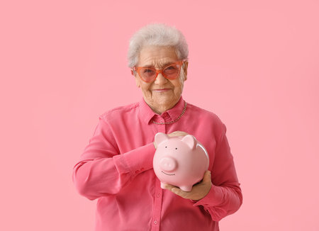Senior woman with piggy bank on pink backgroundの写真素材
