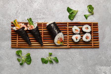 Bamboo mat with tasty sushi cones, rolls and lambs lettuce on grunge backgroundの写真素材