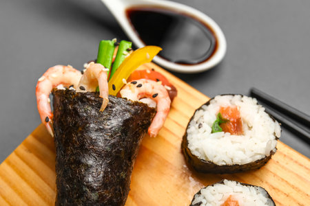 Wooden board with tasty sushi cone, rolls and soy sauce on dark background, closeupの写真素材