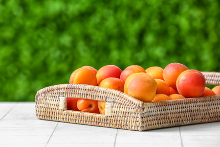 Wicker tray with fresh apricots on white tile table outdoorsの写真素材