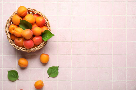 Wicker bowl with fresh apricots on pink tile backgroundの写真素材