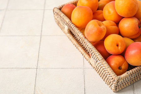 Wicker box with fresh apricots on white tile tableの写真素材