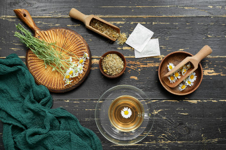 Cup of hot tea and bowl with dried chamomile on black wooden backgroundの写真素材