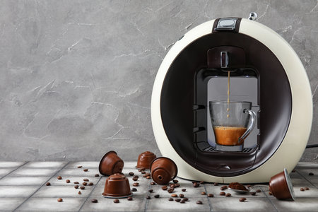 Modern capsule coffee maker with dripping espresso, cup, pods and beans on gray grunge tableの写真素材