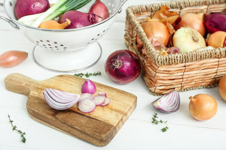Board, colander and wicker basket with different kinds of onion on white wooden backgroundの写真素材