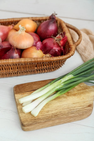 Board and wicker basket with different kinds of onion on white wooden backgroundの写真素材