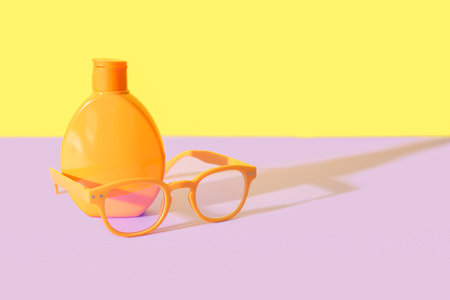 Bottle of sunscreen cream with sunglasses on lilac table near yellow wallの写真素材
