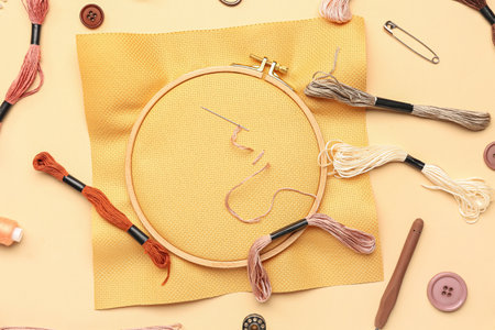 Wooden embroidery hoop with canvas and sewing supplies on pale orange backgroundの写真素材