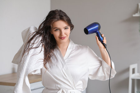 Pretty young woman with hair dryer in bathroomの写真素材