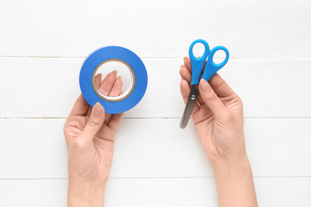 Female hands holding adhesive tape roll and stationery scissors on white wooden backgroundの写真素材