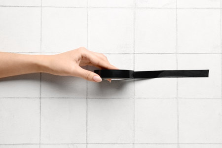 Female hand holding adhesive tape roll on white tile backgroundの写真素材