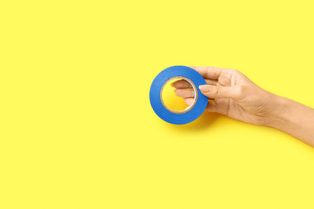 Female hand holding adhesive tape roll on yellow backgroundの写真素材