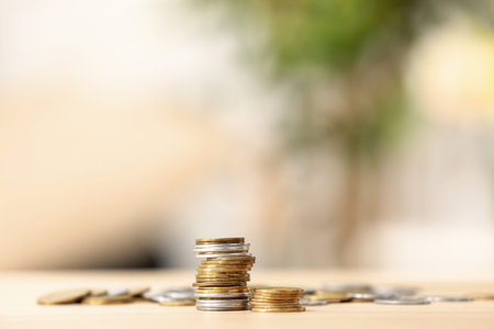 Stacks of coins on wooden table against blurred background