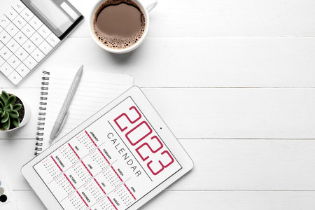 Composition with calendar, cup of coffee and calculator on white wooden background