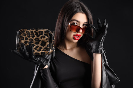 Stylish young woman in leather gloves with bag on dark background, closeupの写真素材