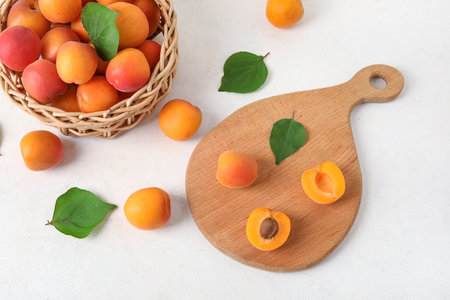 Board and wicker bowl with fresh apricots on white tableの写真素材