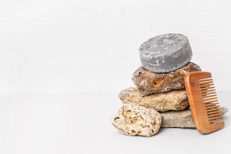 Gray solid shampoo bar with stones and comb on table near white wall