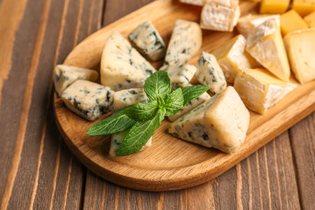 Board with pieces of tasty cheese on wooden background, closeupの写真素材