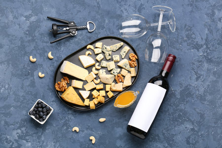 Pieces of tasty cheese, honey, glasses and bottle with wine on blue backgroundの写真素材