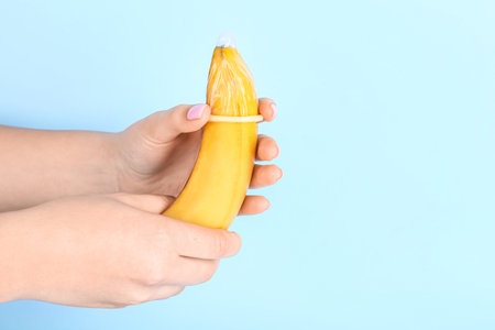 Woman putting condom on banana against blue background. sex conceptの写真素材